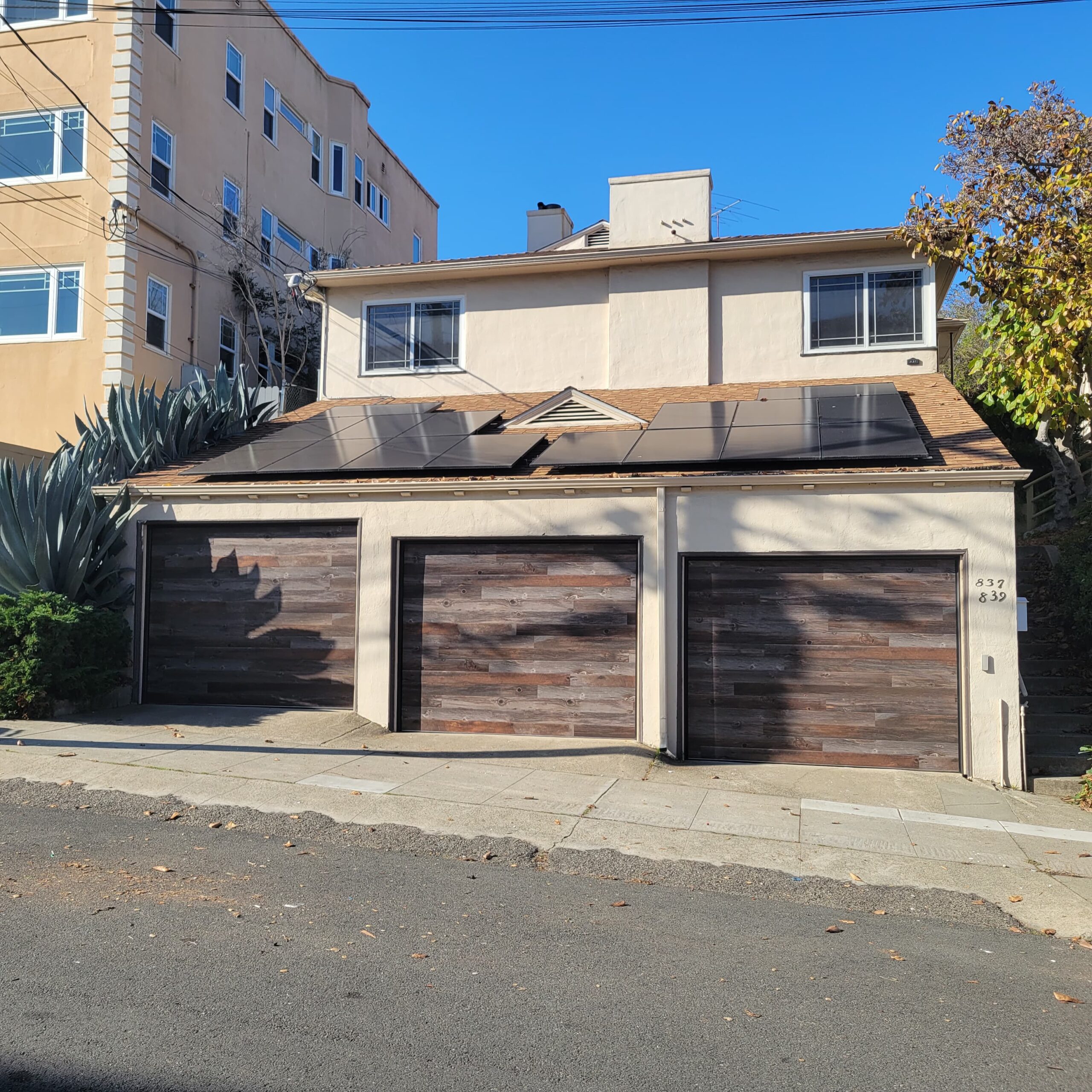 Three wooden garage doors on a house with solar panels and agave plants.