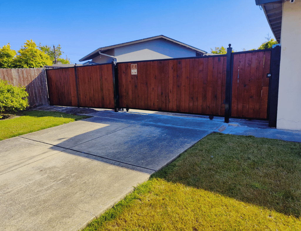 A dark brown wooden gate with black metal posts and a concrete driveway.