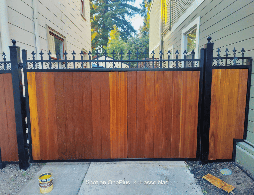 A wooden fence with black metal accents between two buildings.