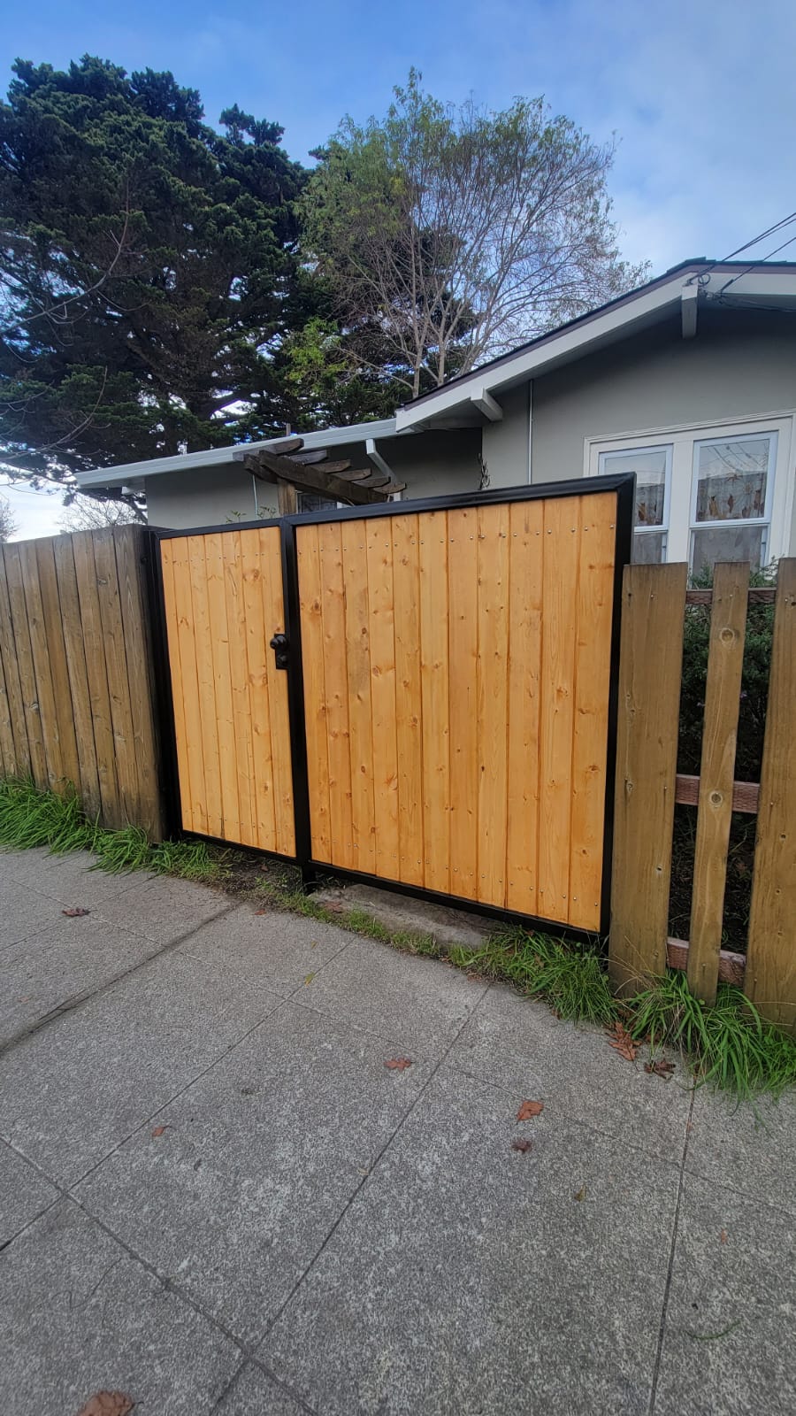 New wooden gate with black frame next to a house and fence