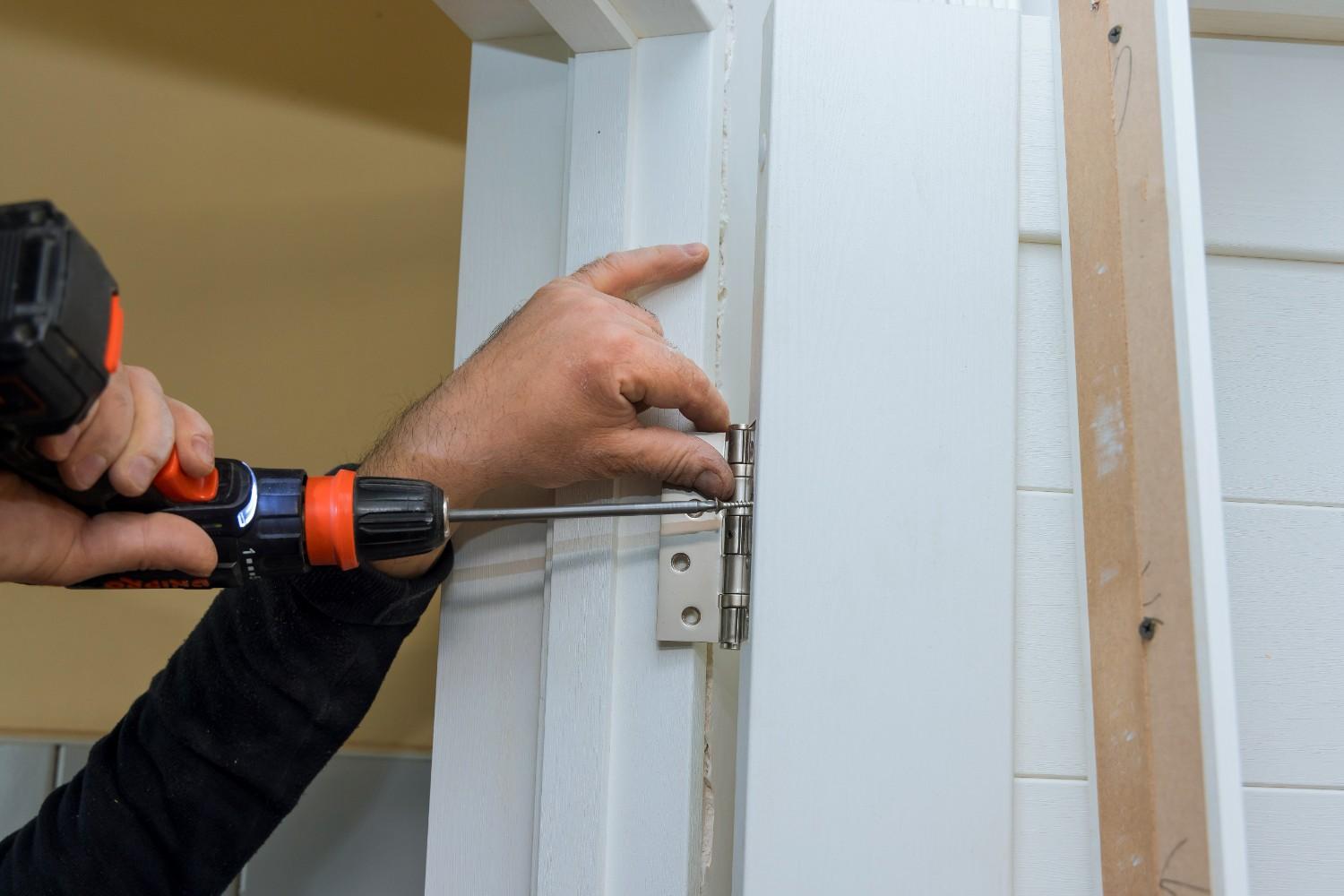 Close-up of hands installing a door hinge with a screwdriver.