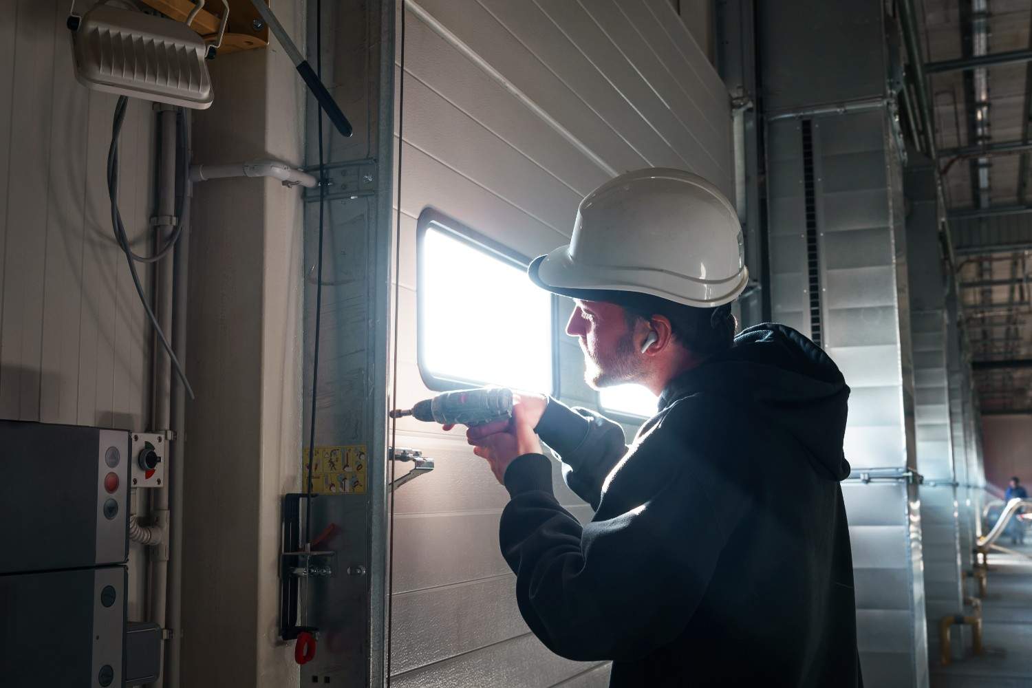 Man in hard hat using a power drill on a garage door.