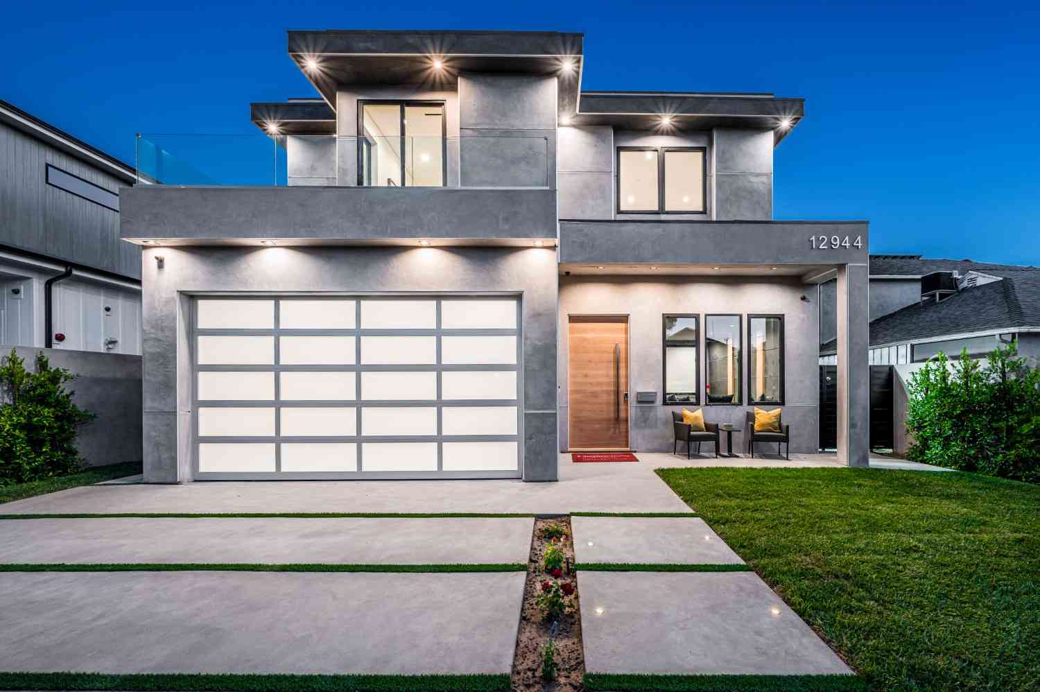 Modern gray house with a two-car garage and illuminated exterior at dusk