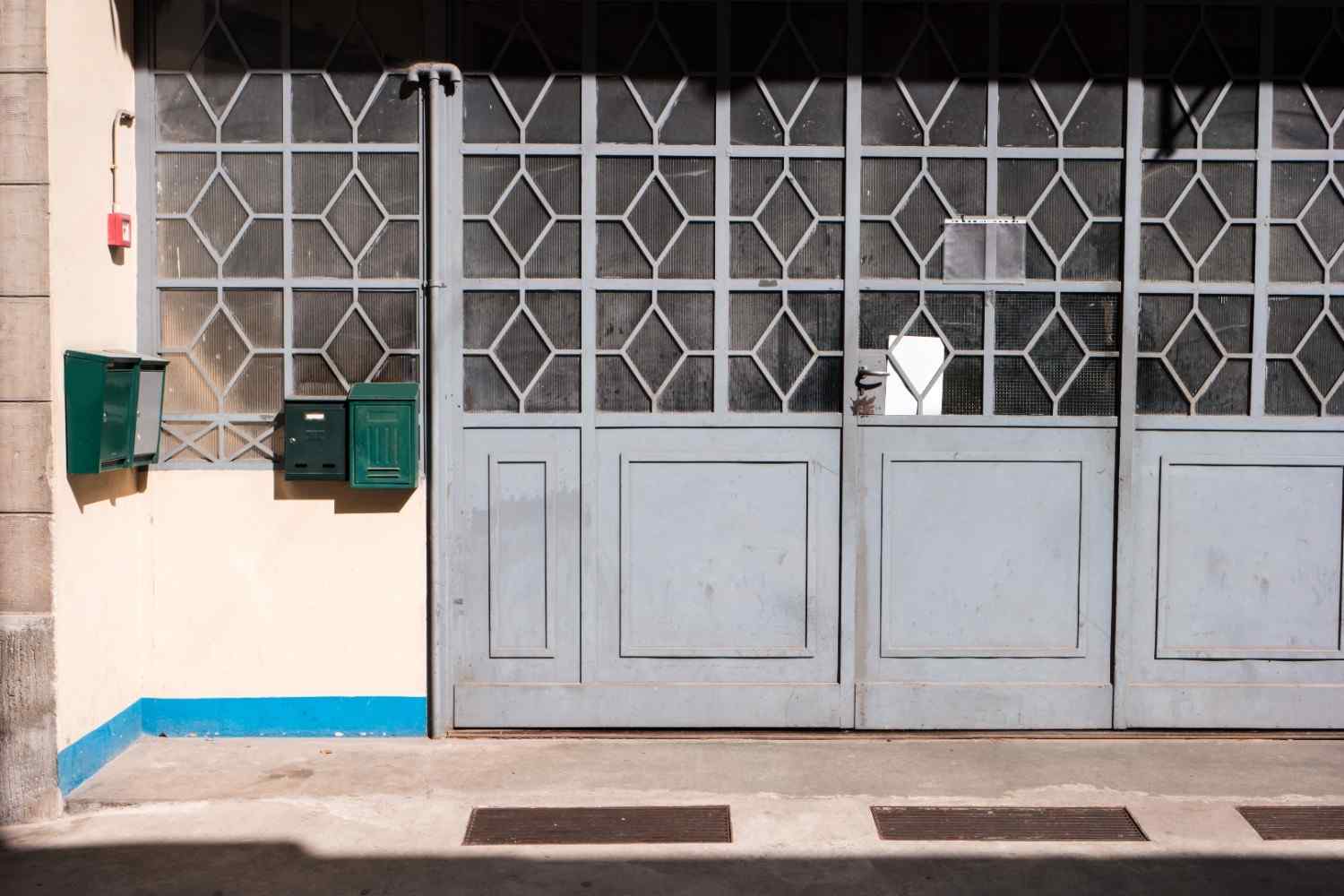 Two green mailboxes on a wall next to a large gray metal door