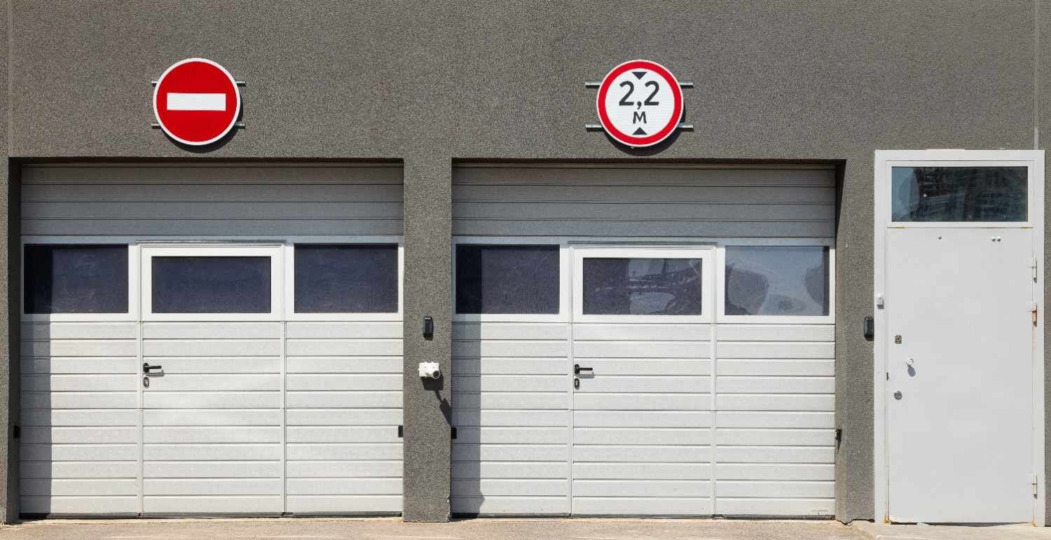 Two garage doors and a white door on a gray building