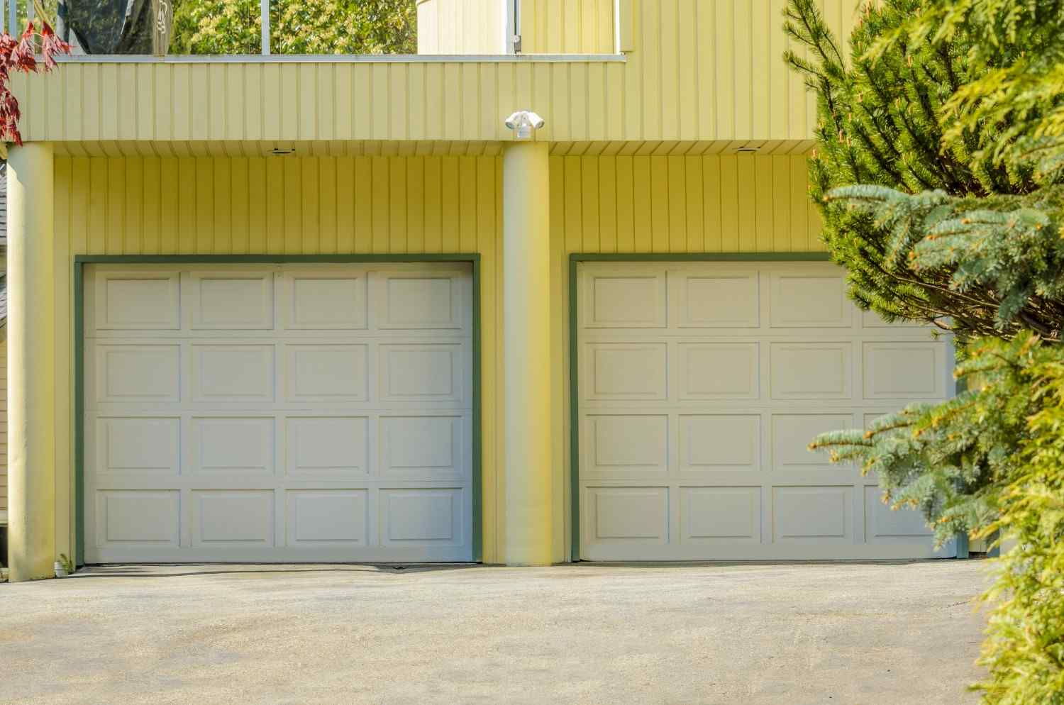 Two white garage doors on a yellow house with green trim.