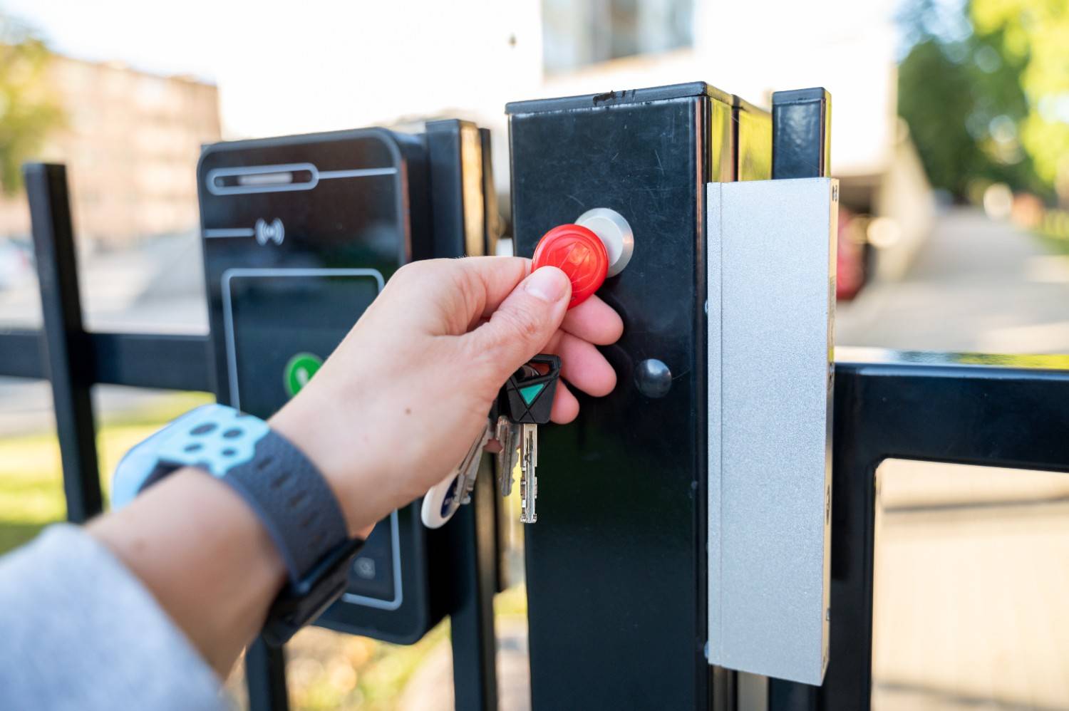 Hand using a red key fob to open a black gate