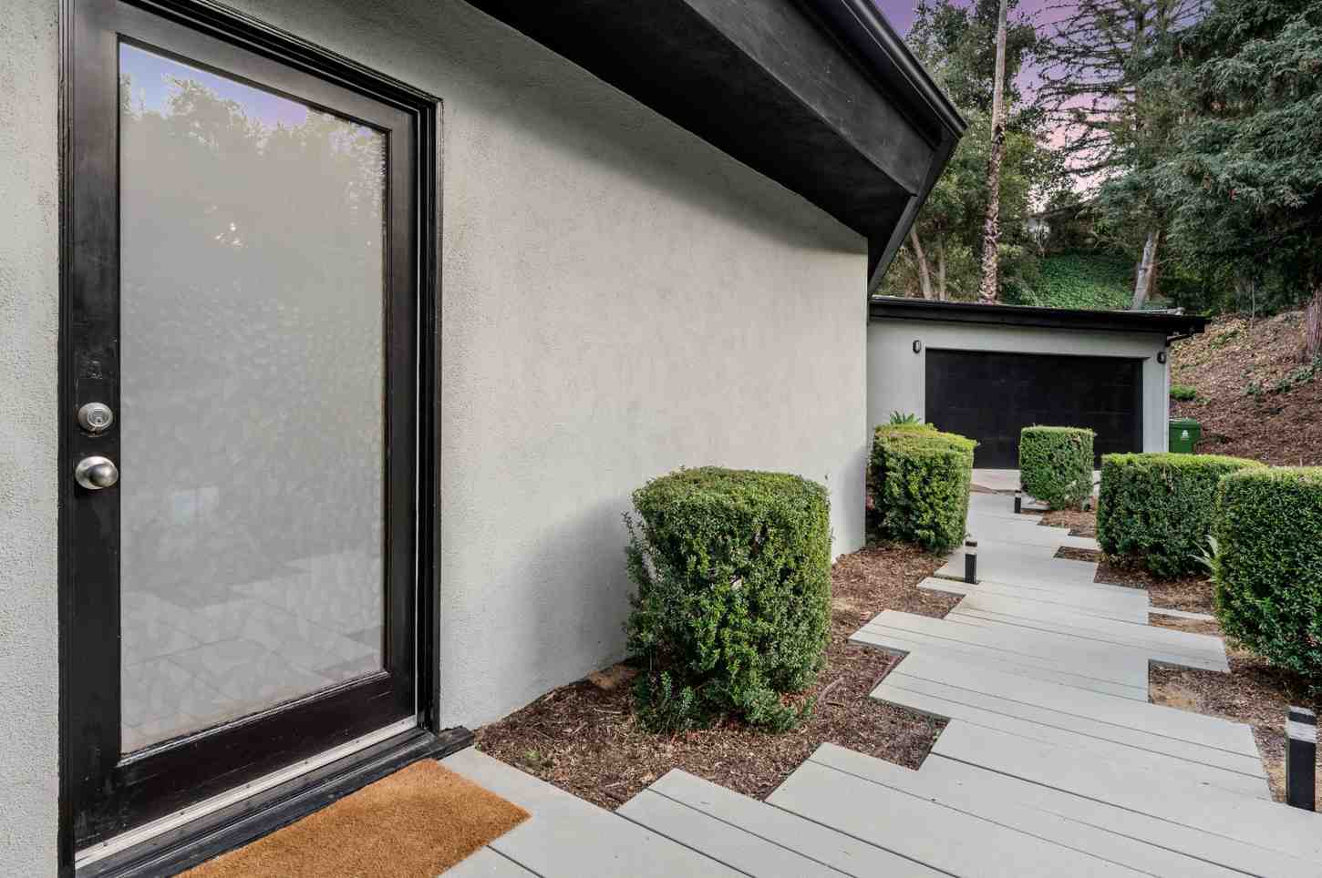Modern home entrance with dark door, light gray walls, and landscaped path.