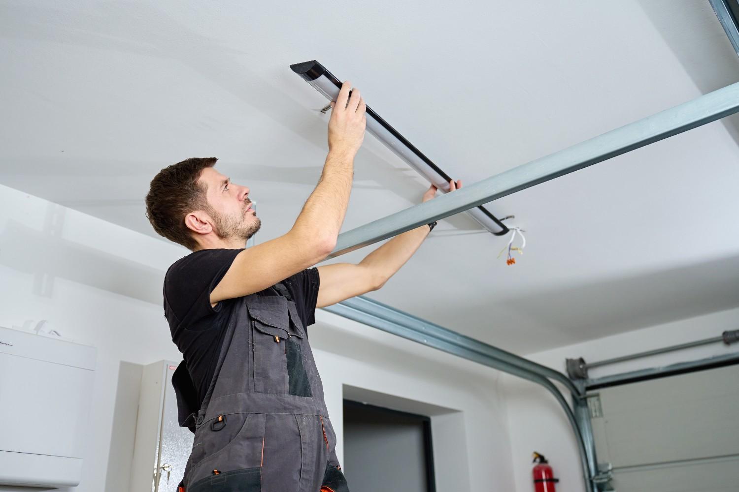Man installing a long light fixture on a white ceiling in a garage