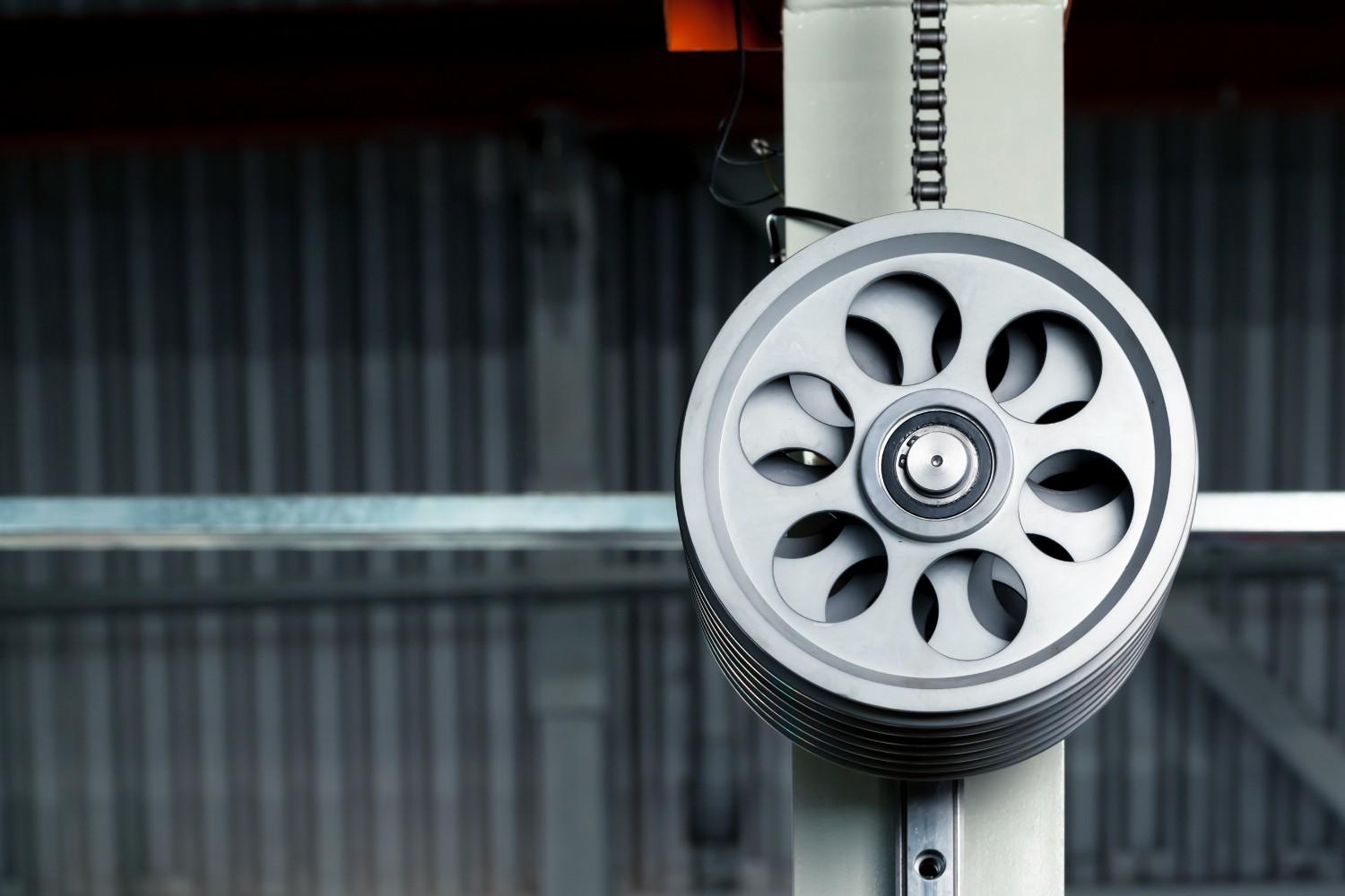 Close-up of a large, gray industrial pulley wheel with a chain.