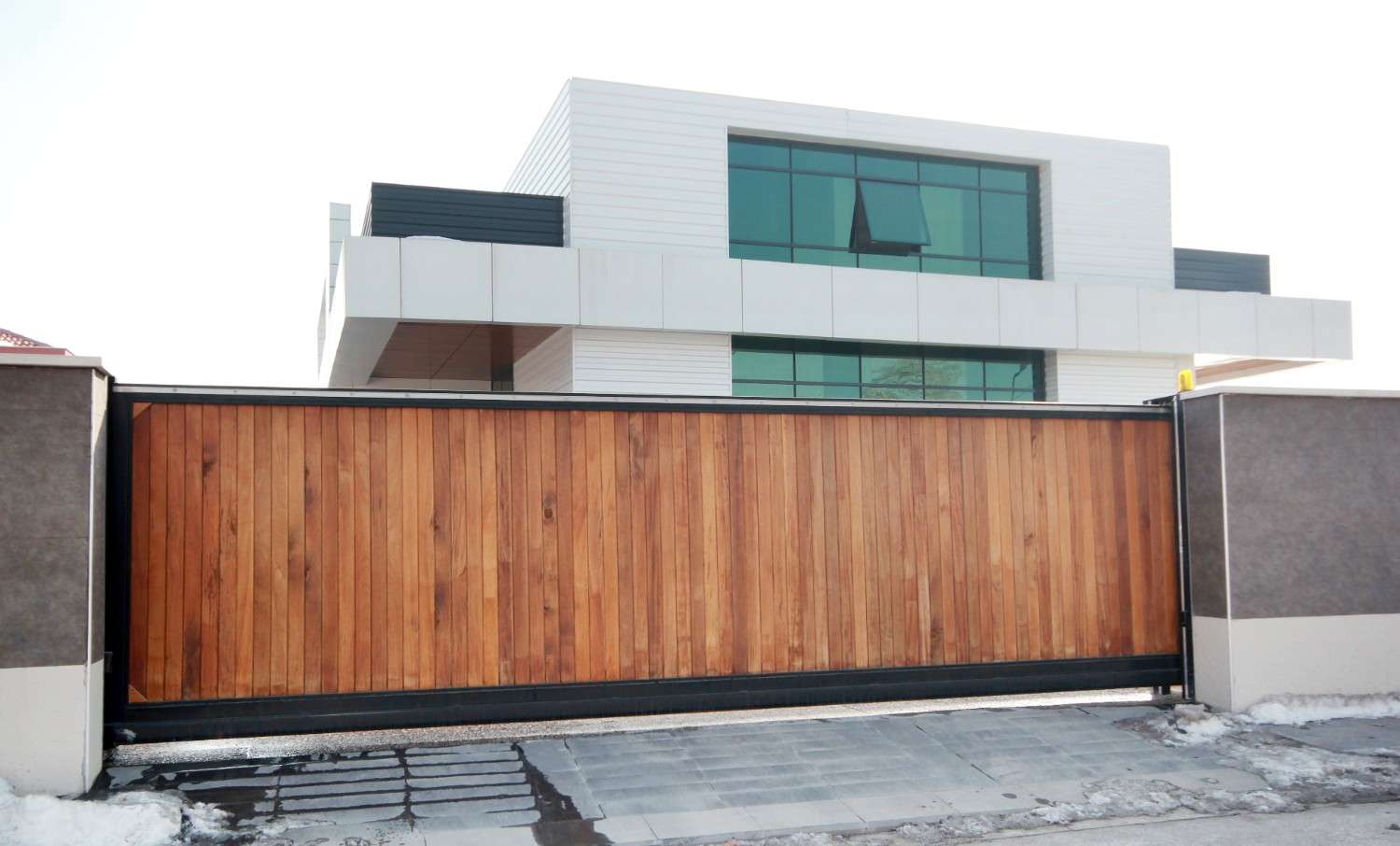 Modern house with a large wooden sliding gate and snow on the ground