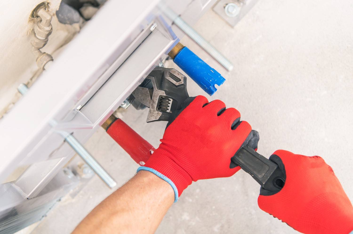 Person in red gloves tightening plumbing with a wrench