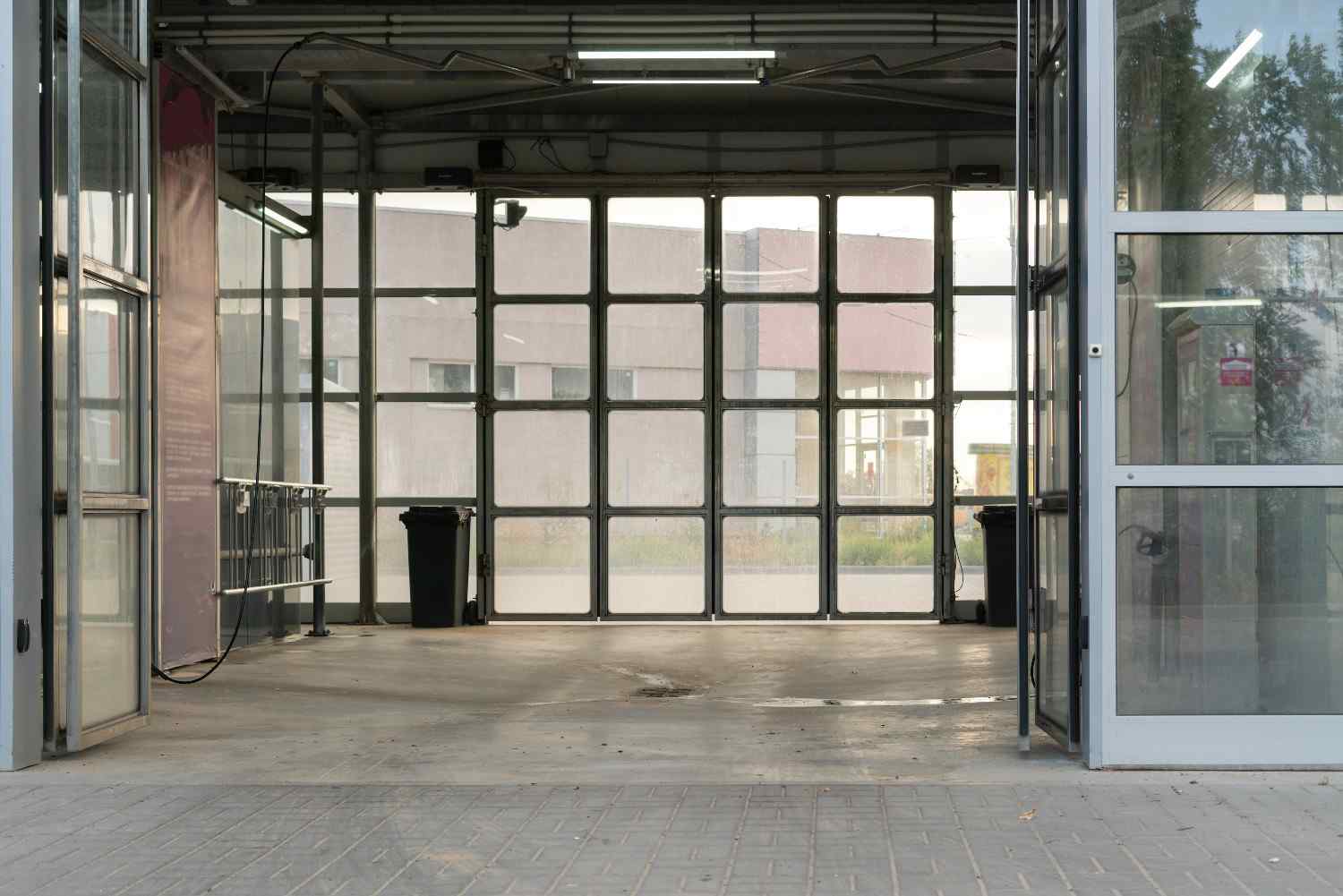 Empty garage interior with large glass doors and two black bins.