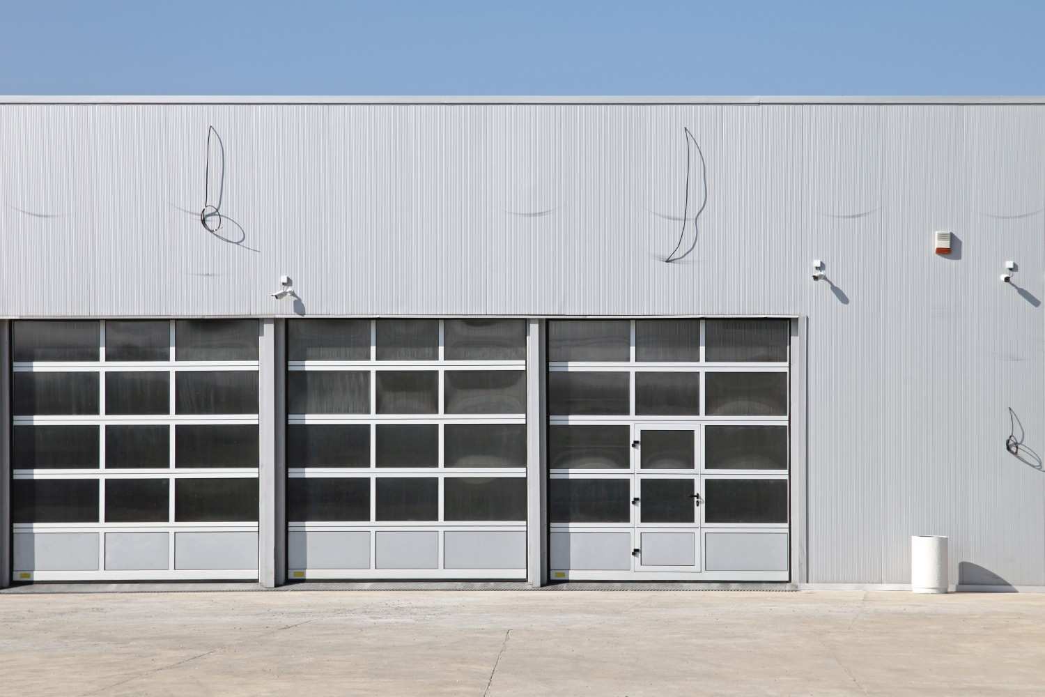 Three large garage doors on a light gray industrial building under a clear sky.