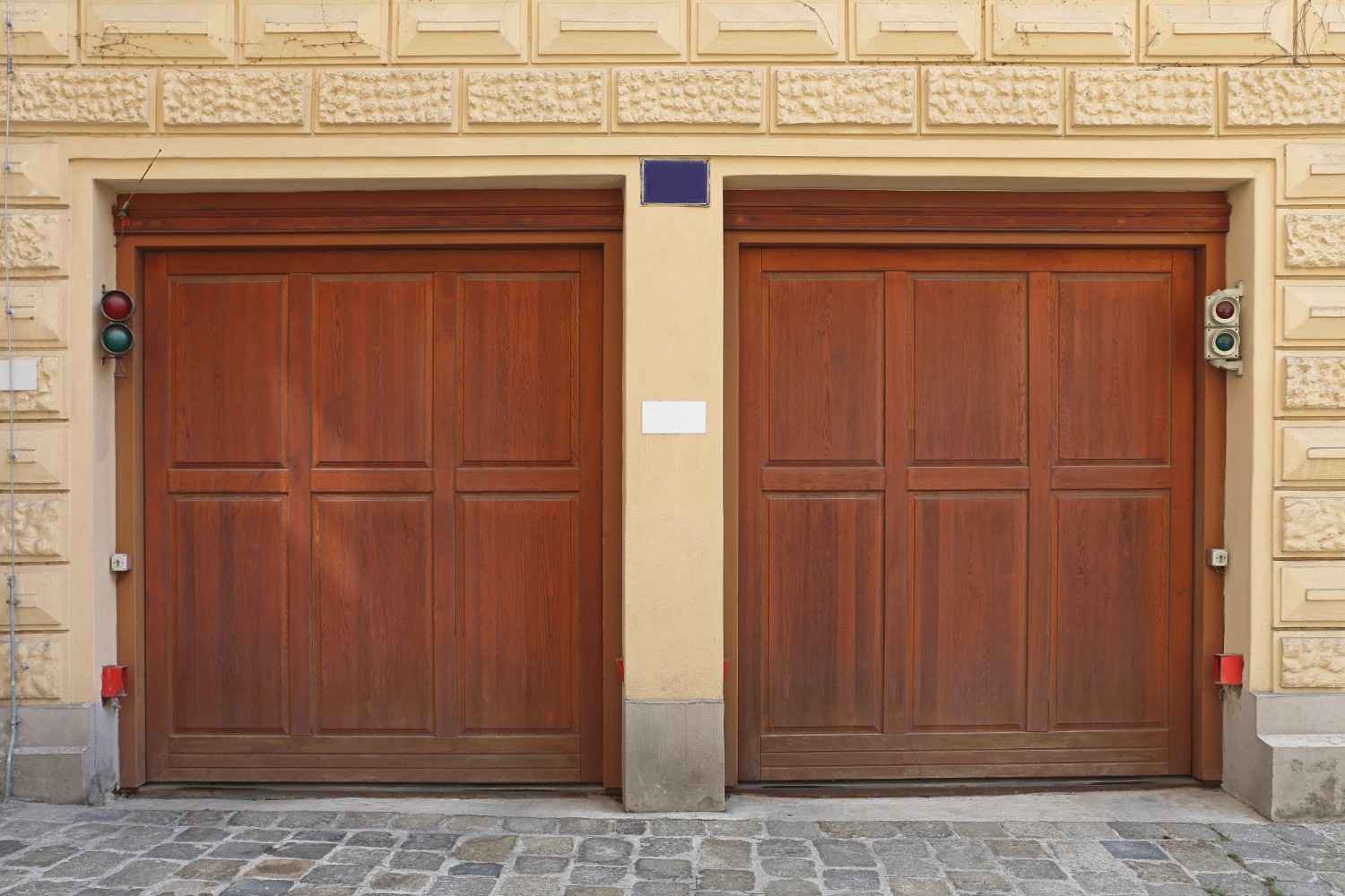 Two brown wooden garage doors with traffic lights on a stone wall.