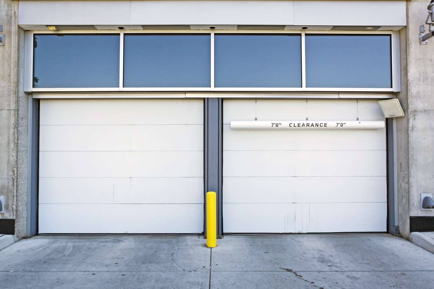 Two white garage doors with a yellow safety bollard in front
