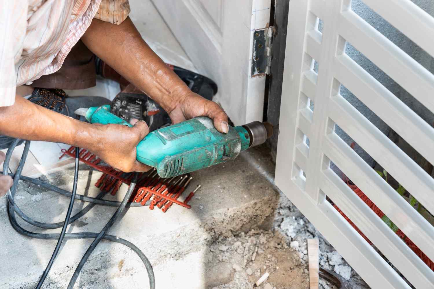 Man drilling a hole in a white metal gate with a power drill.