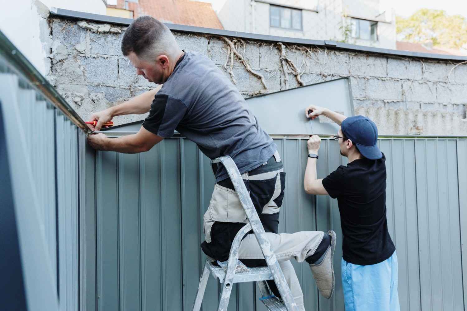 Two men installing a metal fence outdoors